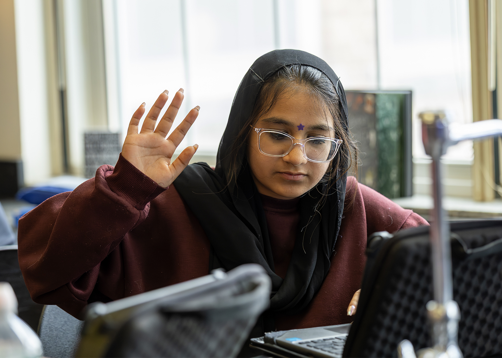 student raising hand in science class while sitting at chromebook