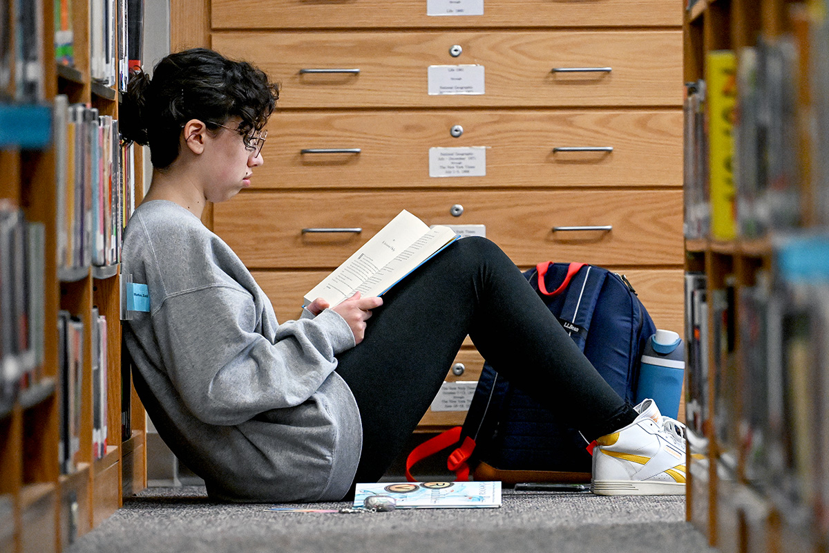 Female High School student reads on the floor of the library.