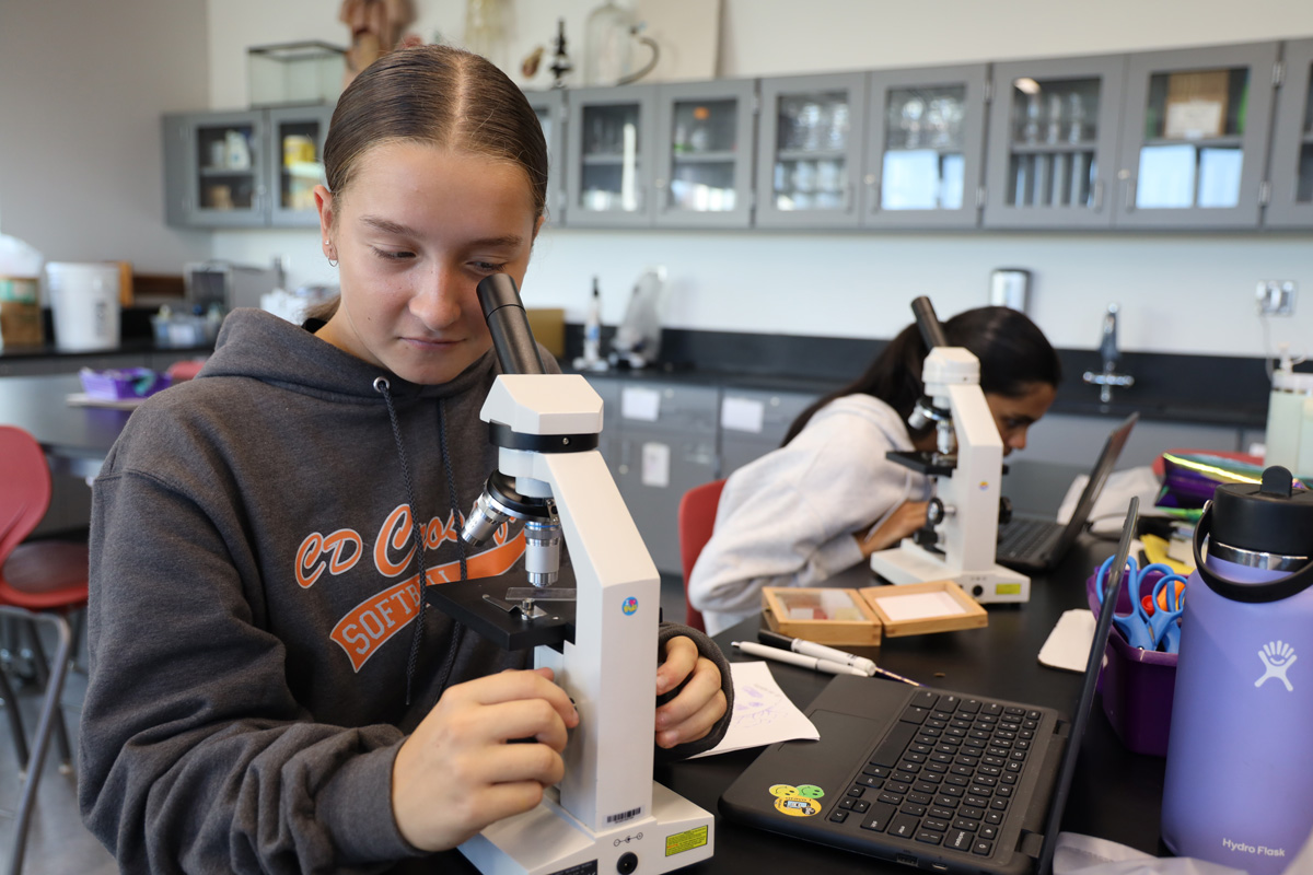 A teen peering into a microscope in a lab setting.