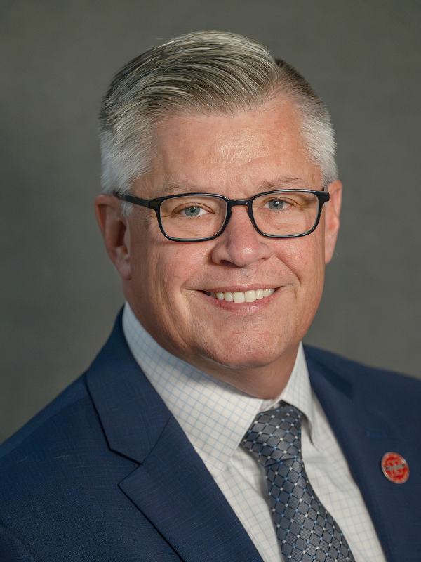 Professional photo of Carl Mummenthey, smiling wearing a navy suit with a gray blue tie