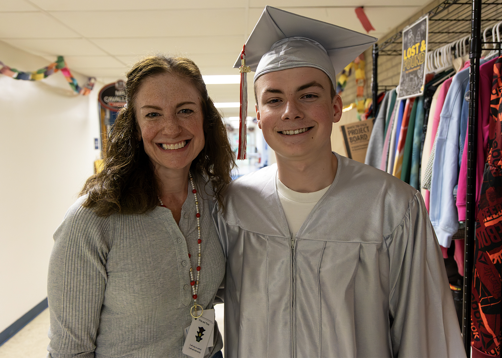 mom and gradaute, who is wearing cap and gown, in hall of elementary school
