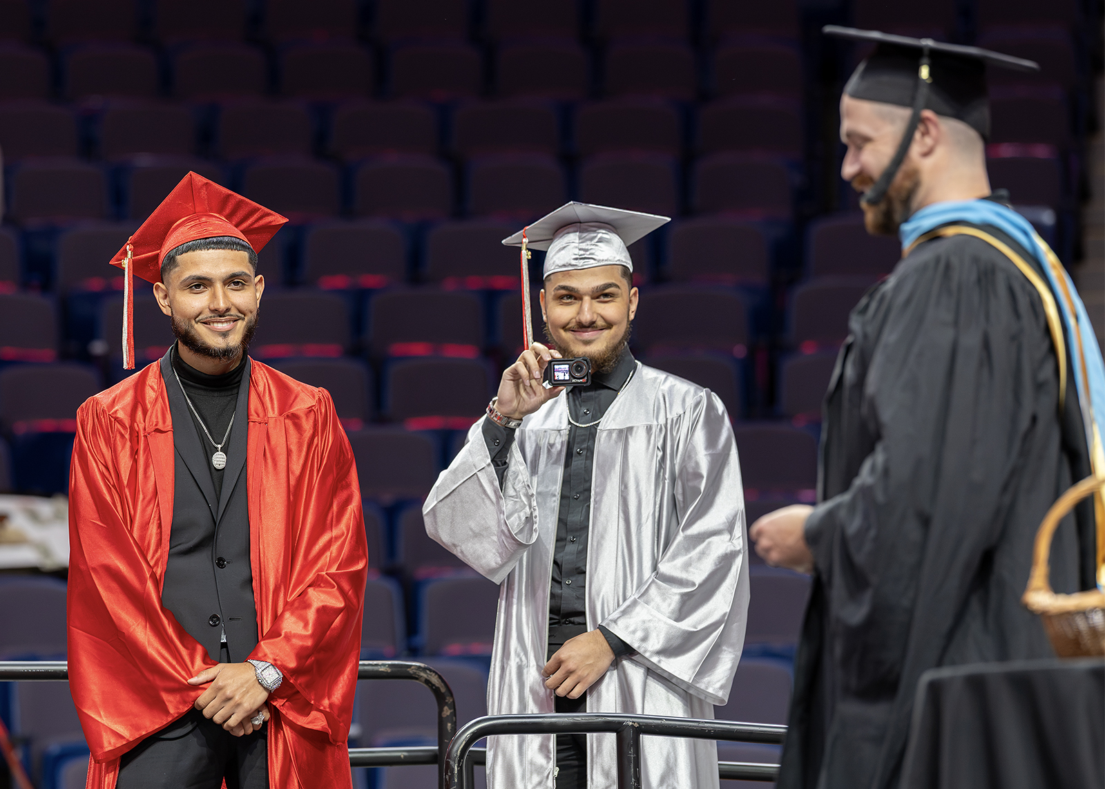 two graduate smile a an assistant principal on stage at graduation