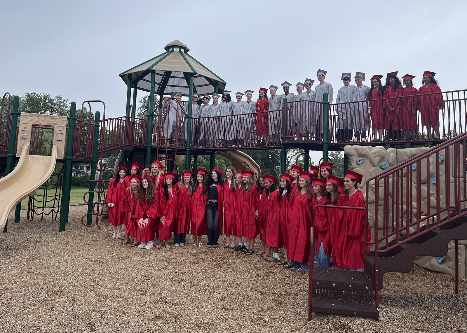 group of graduating seniors on an elementary playground in their caps and gowns
