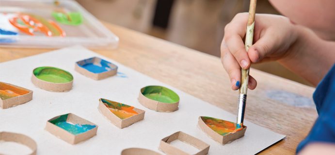 Close-up photo of a student painting basic shapes that are outlined by cardboard