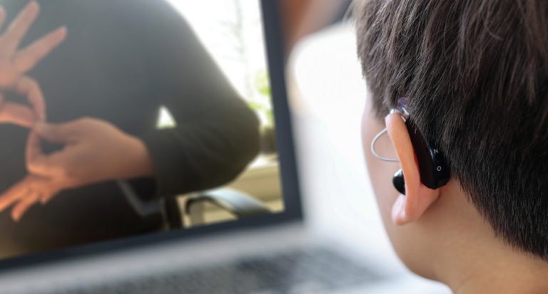 Close-up of a hearing aid on a student who is watching a teacher use sign language