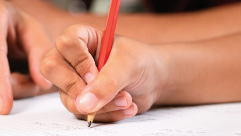 Close up photo of a hand holding a pencil and writing on lined paper