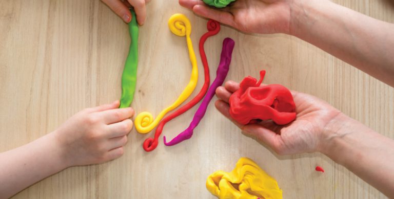 Close up of hands playing with clay. Some of the clay is held in lumps and some has been rolled into strips.