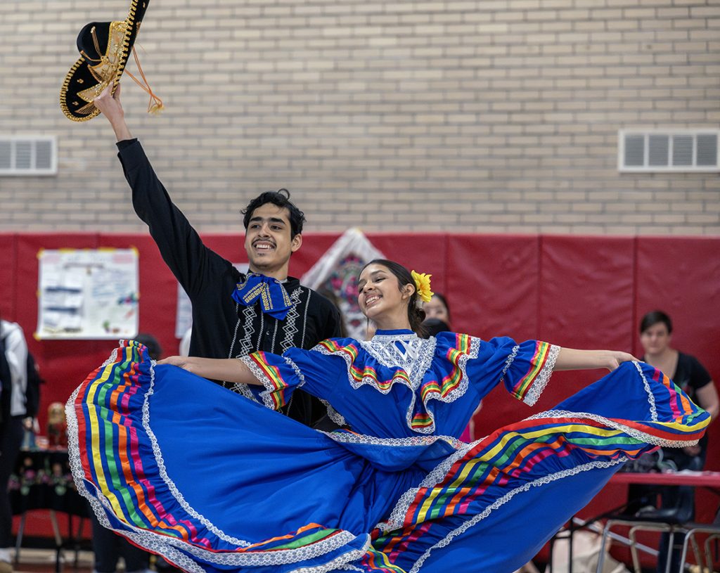 Two dancers in cultural costume performing in a gym setting.