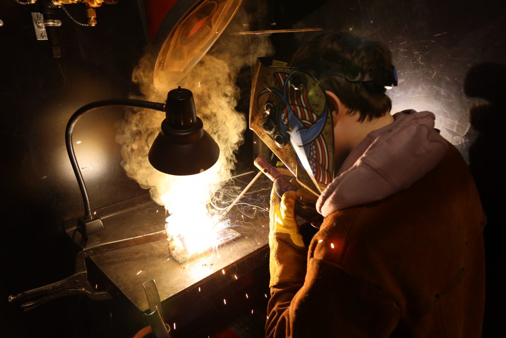 A high school student welding with protective gear.