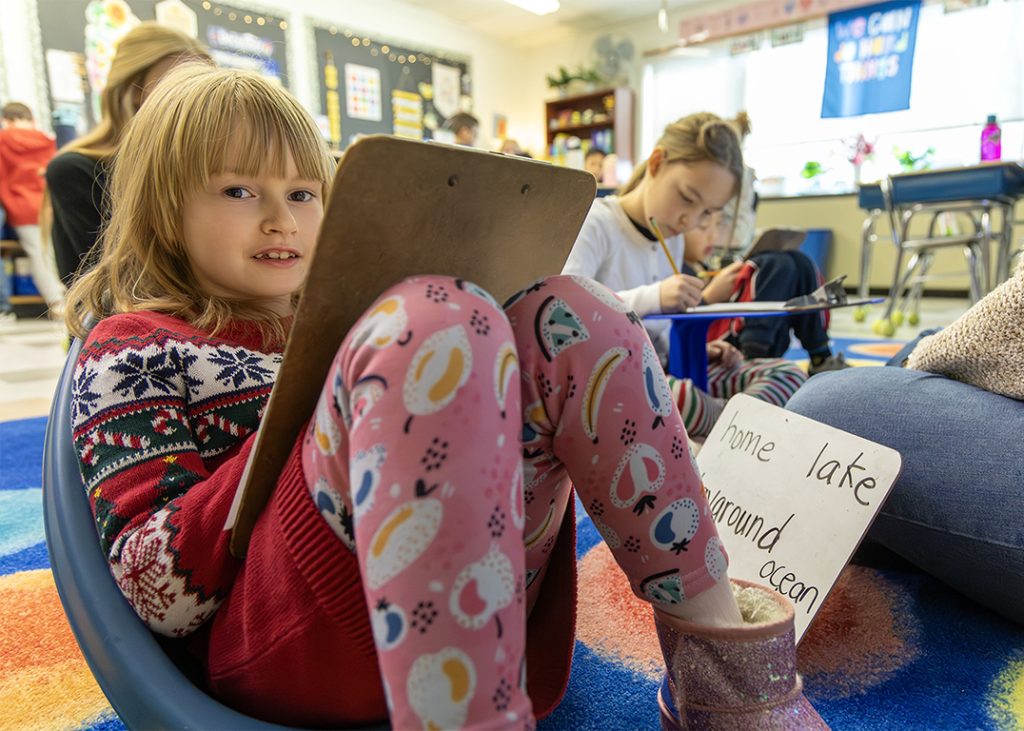 Close-up photo of students doing work while sitting on bean bags. The students are holding a whiteboard and practicing their writing