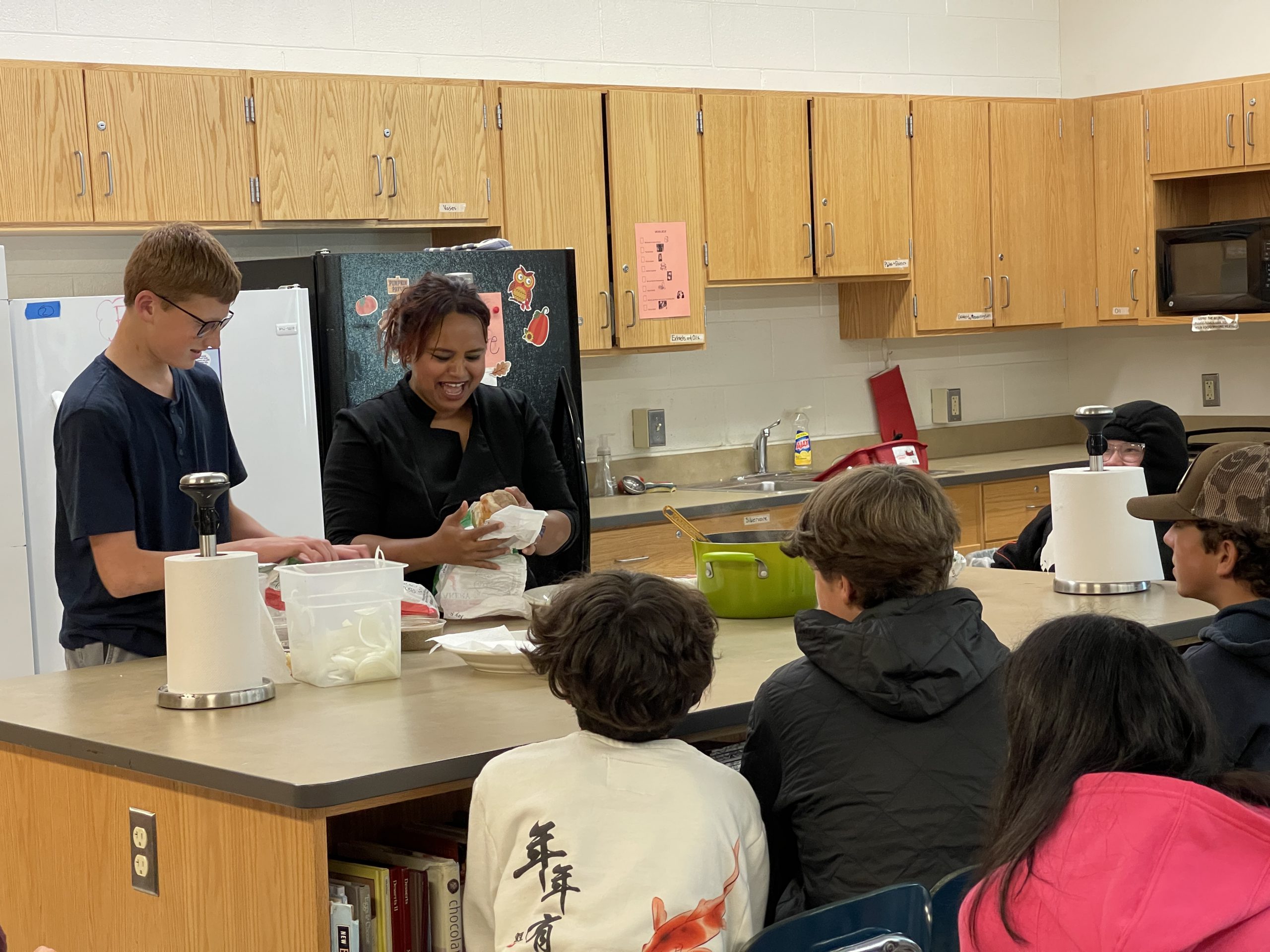 Students watching food being prepared in a classroom kitchen.