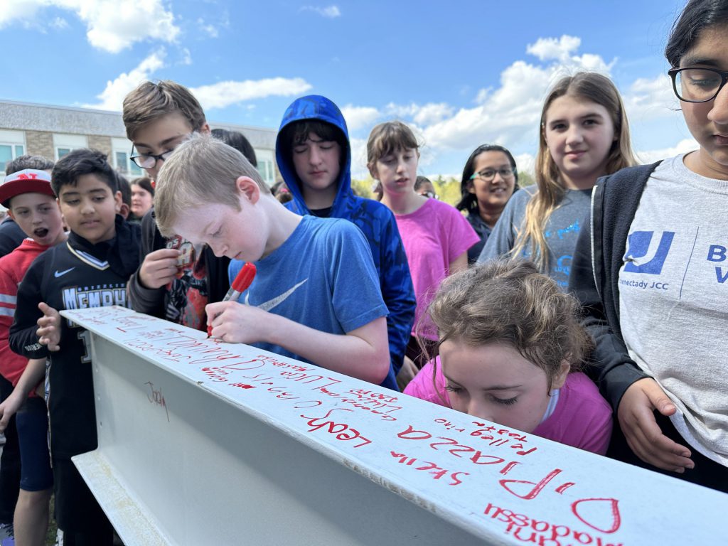 Students crowd around to sign a steel beam.