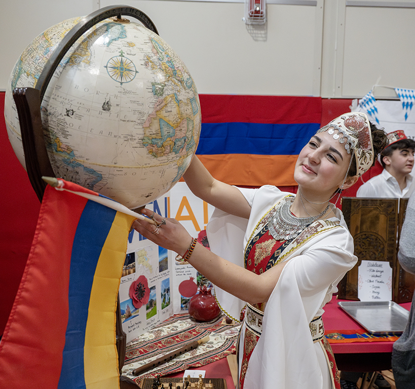 A student dressed in cultural costume holding up a globe.