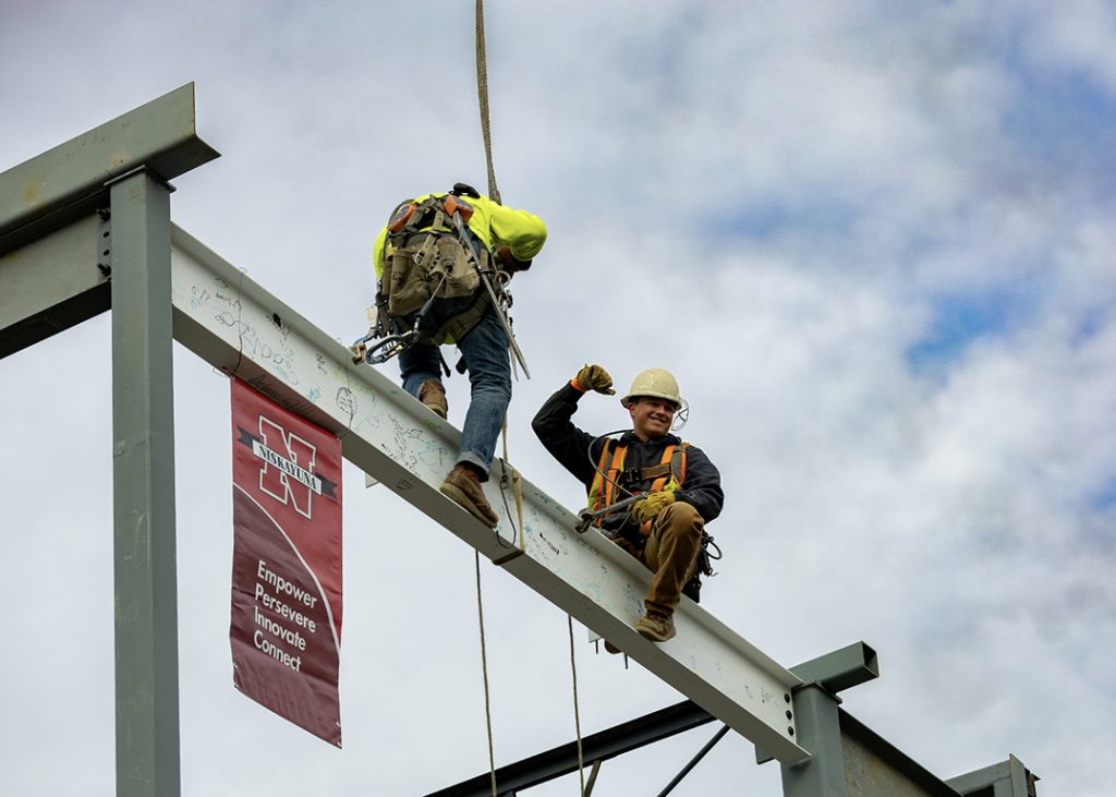 Construction workers high on a steel beam with a Niskayuna school district banner.