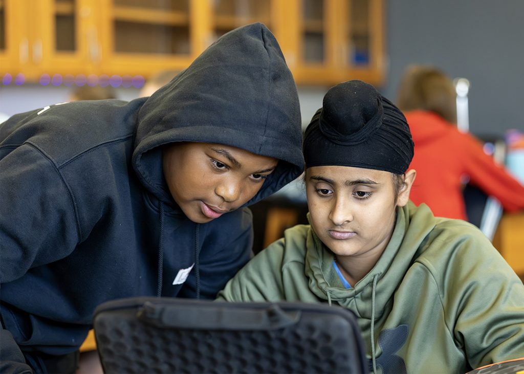 Two students peer into a laptop.