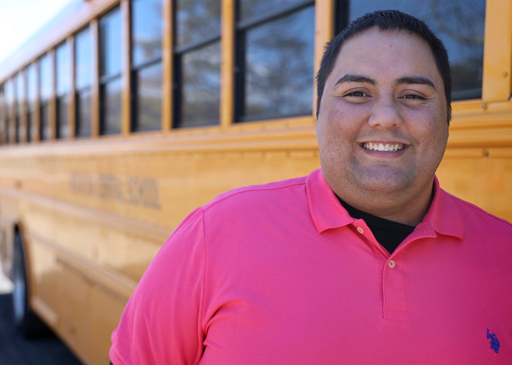 A happy bus driver stands near a school bus.