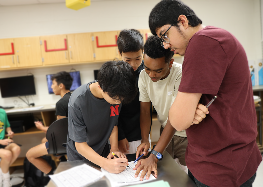 high school students gathered around to complete a worksheet.