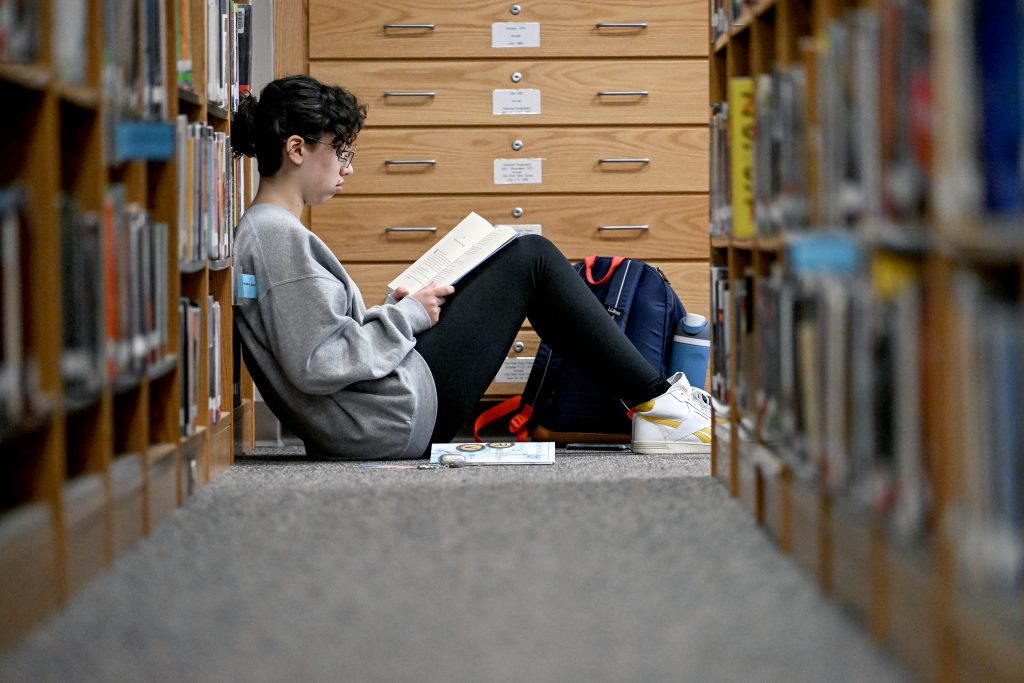 A student sitting on the floor of a library reading.