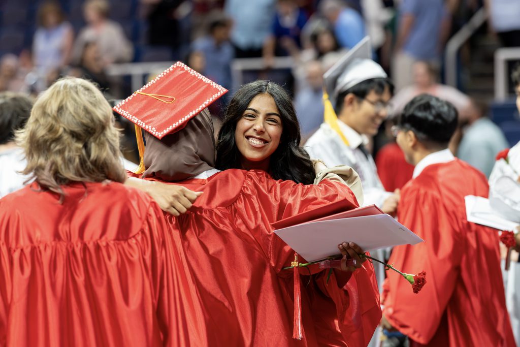 A graduate hugs another graduate during graduation.