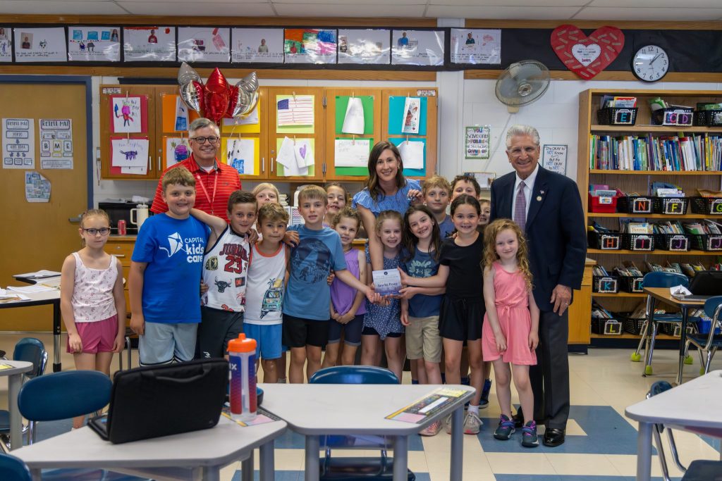 A group of young elementary students and adults standing together and posing for a group photo inside a classroom setting.