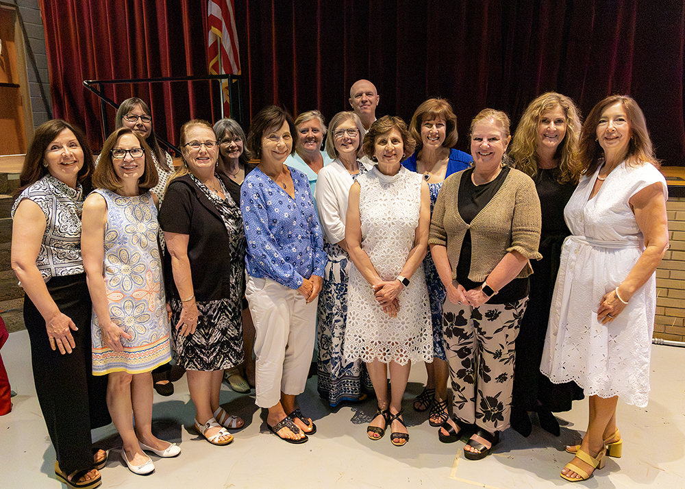 A group of retirees posing together for a group photo on a stage with red curtains in the background.