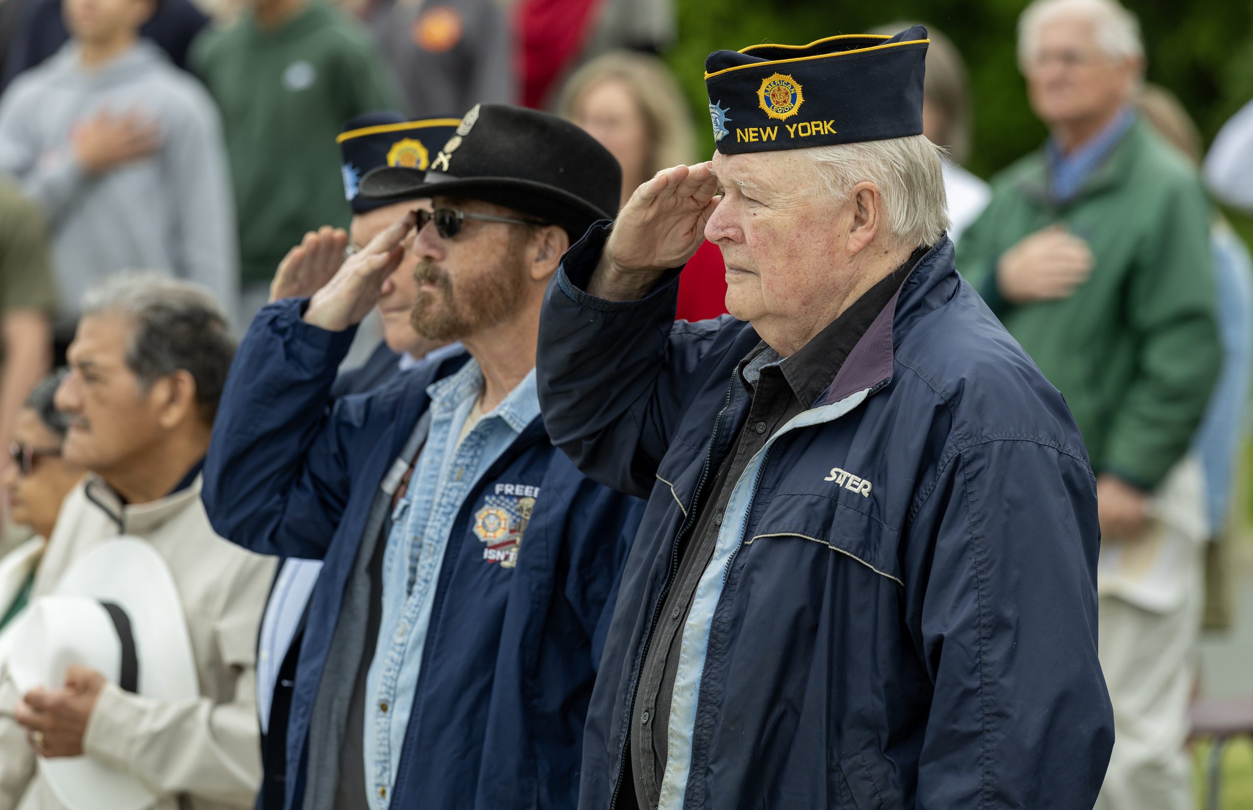 Several adults saluting while others place their hands over their hearts.