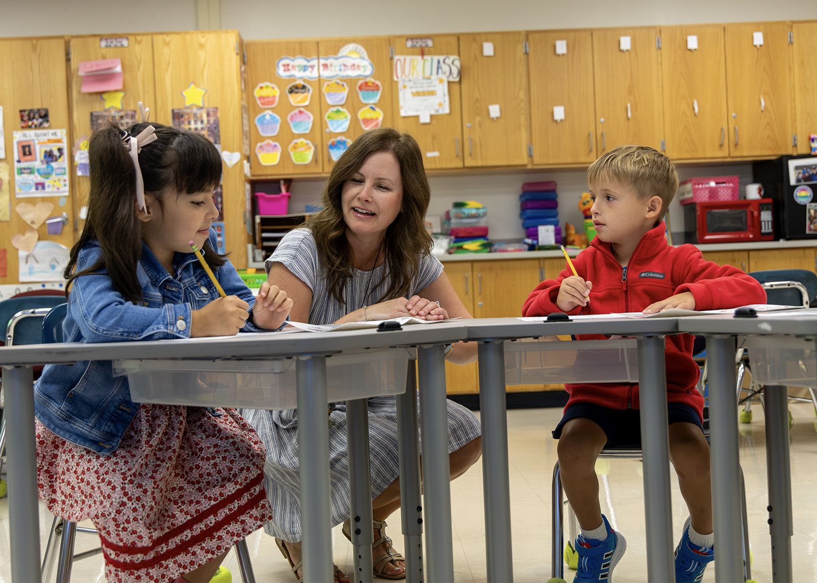 teaching helping two elementary students at desk