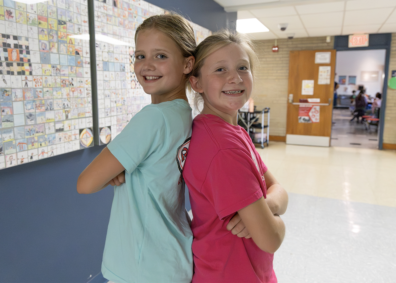 two elementary friends smile back to back with arms crossed