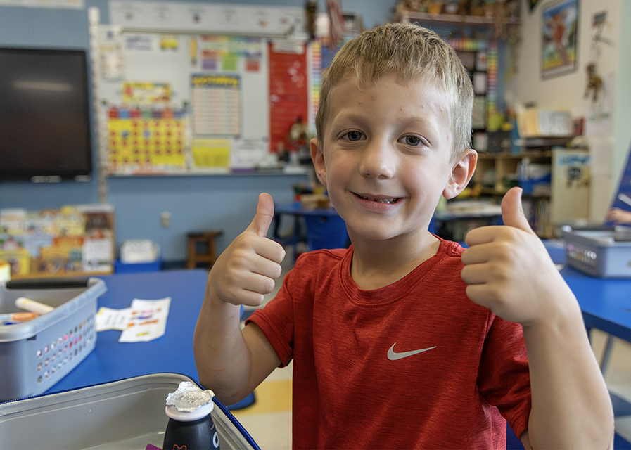 A student displays two thumbs up in a classroom.