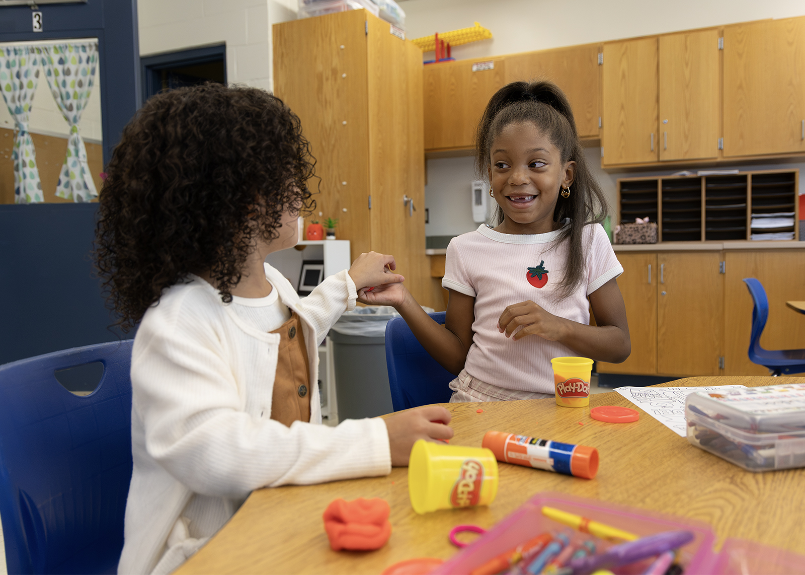 two elementary students smiling and playing with play-doh