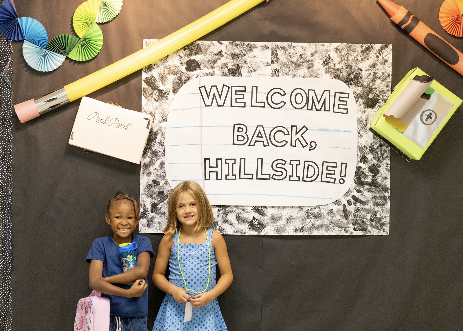 two elementary students smile in front of a sign that says welcome back hillside