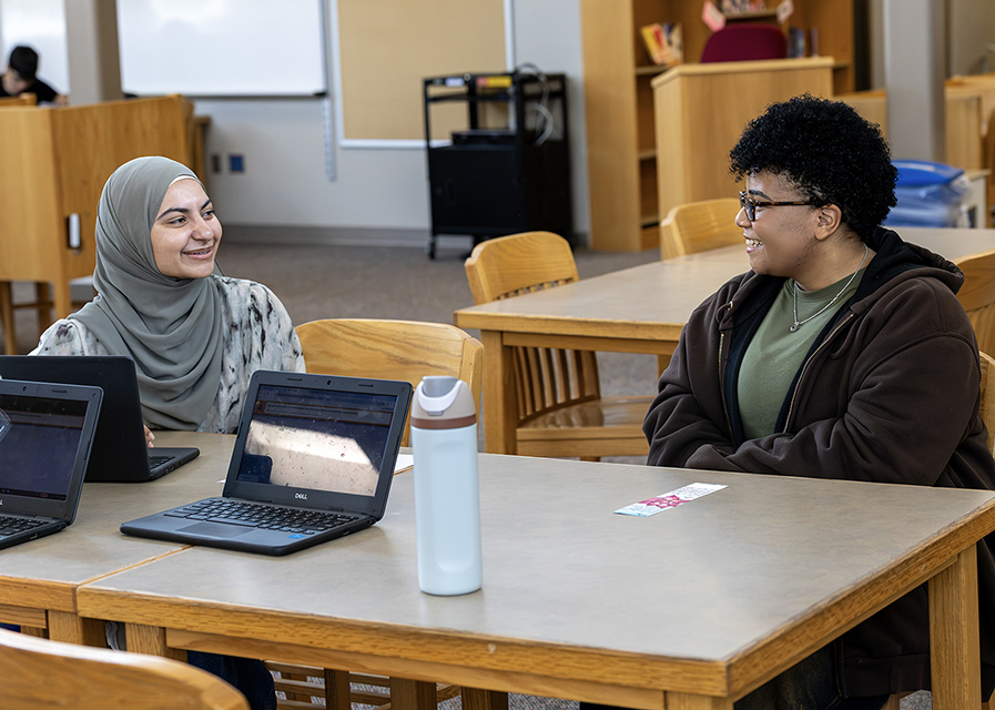 Two teens chatting in a classroom setting.