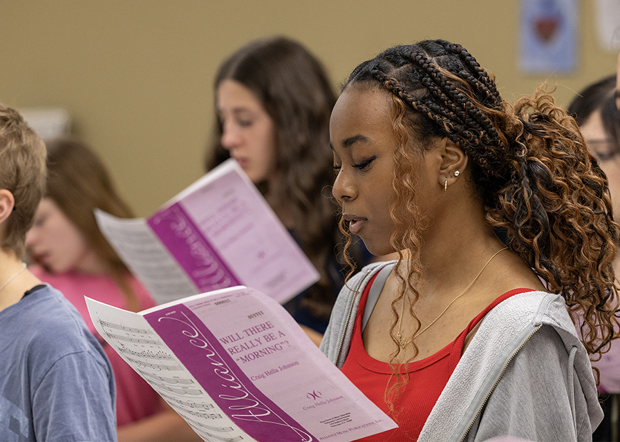 Choir students sign while holding sheet music.