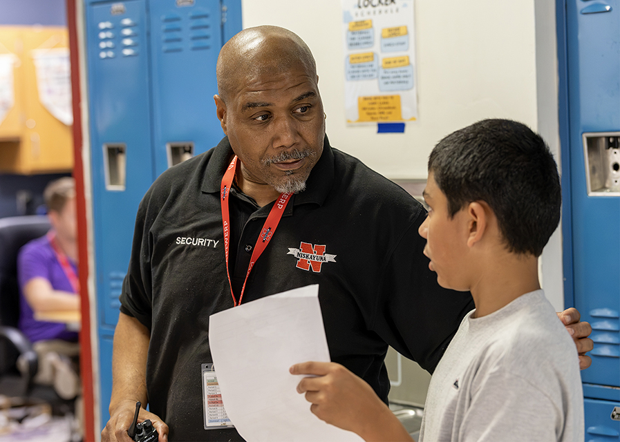 A teacher listens to a student in a hallway.