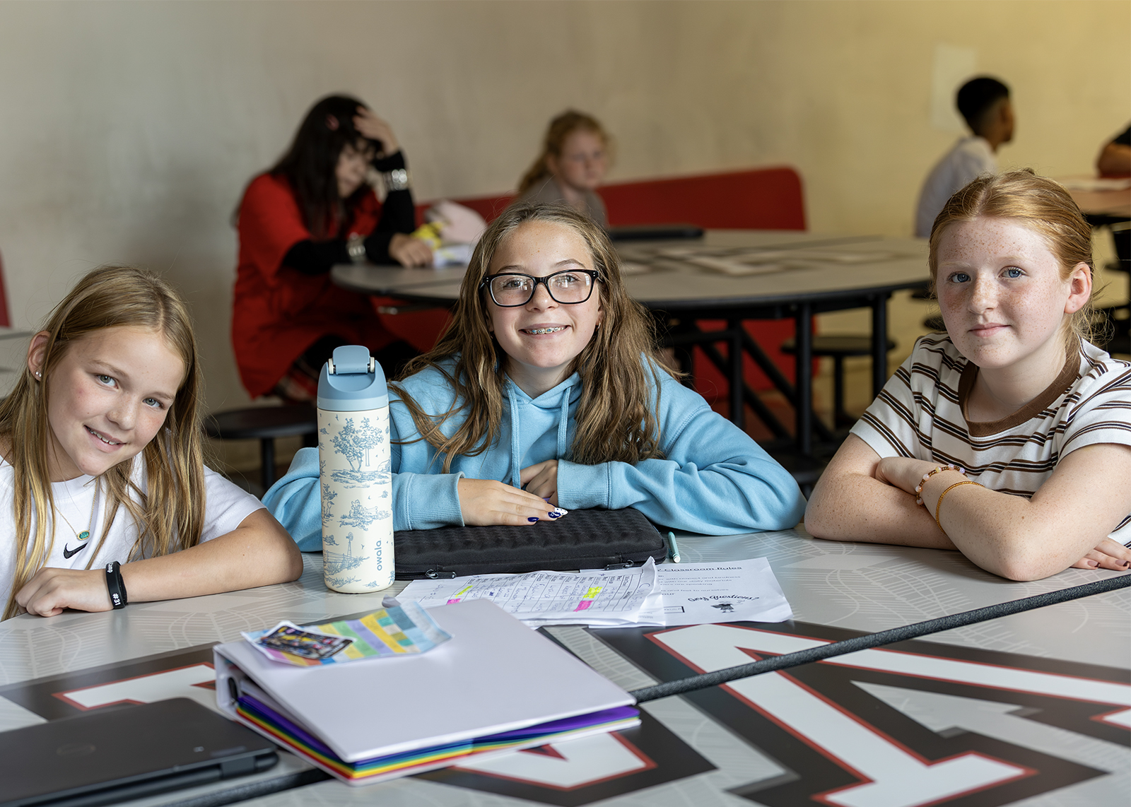 three middle school students at cafeteria table smiling