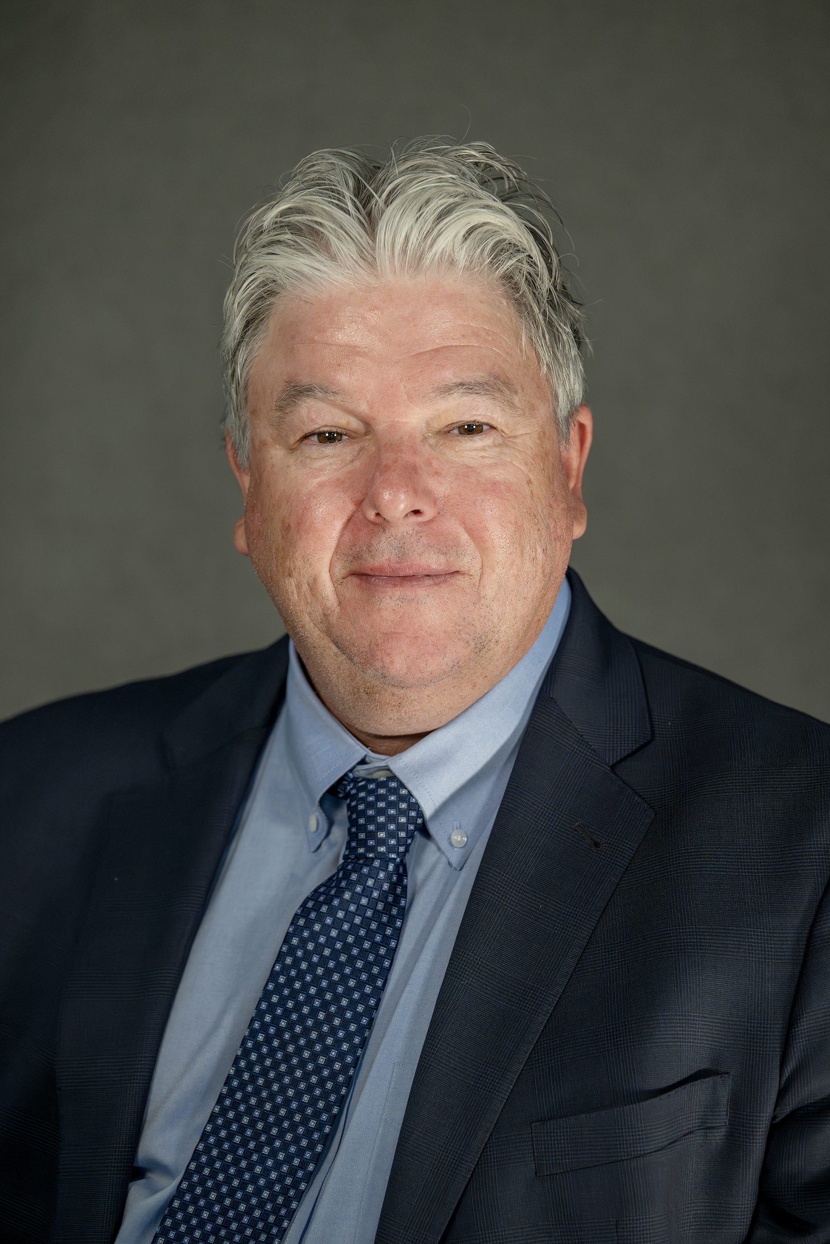 Professional headshot of Bill Anders wearing a dark suit jacket, navy tie, and light blue dress shirt.