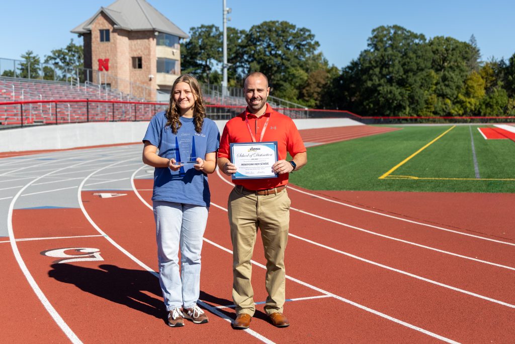 Athletic Director Matt Ronca stands with student on track, both hold awards.